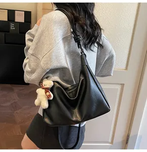 Detail of black leather hobo bag with knotted strap and cute plush bear charm on side