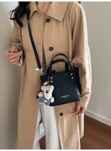 Détail du sac seau noir avec lettrage de marque et breloque peluche ours bleu