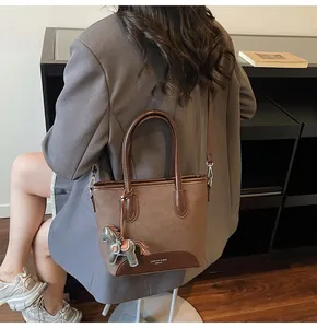 Detalle de un bolso cubo marrón con colgante de caballo de cuero y logotipo grabado