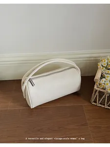 Detail of minimalist cream leather barrel bag with smooth handle and metal zipper