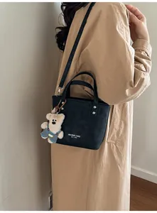 Vue détaillée du mini sac seau noir avec pendentif ours porté sur un trench-coat kaki