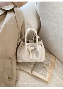 Detail of minimalist cream bucket bag with leather strap and buckle on trench coat