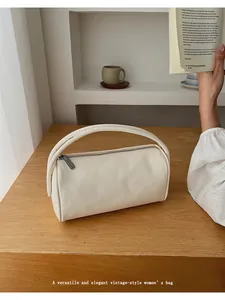 Minimalist beige cylinder handbag on a wooden desk with a ceramic cup and books