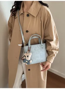 Détail du sac à main en similicuir bleu clair avec logo imprimé et breloque ours sur trench
