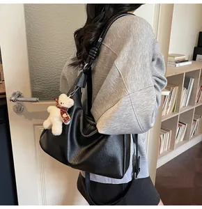 Close-up of black crescent shoulder bag with white teddy bear charm accessory