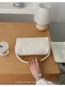 Detail view of white vintage-style leather bag on wooden table with elegant accessories