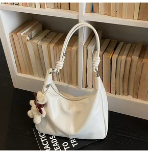 Detail of off-white hobo bag showing knotted shoulder strap and plush bear charm