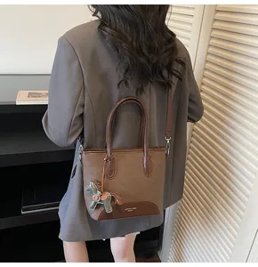 Detalle de un bolso cubo marrón con colgante de caballo llevado al hombro por una modelo