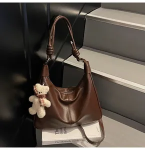 Close-up of deep brown leather tote with knotted strap and cute plush bear charm decoration