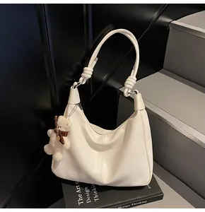 Detail of a creamy white hobo bag featuring knotted strap and cute bear charm on books