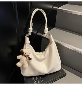 Detail view of cream PU leather hobo bag with stitched lines and plush bear charm