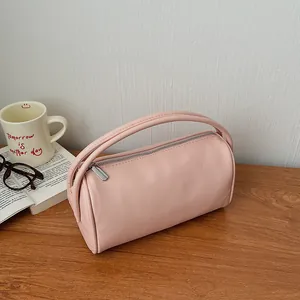 Minimalist pink lychee leather cylinder handbag with top handle on a wooden table