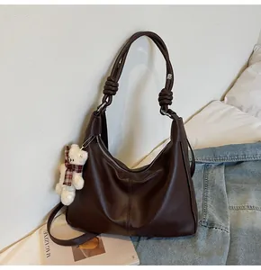 Detail of dark brown tote bag with decorative shoulder strap knot and white teddy bear charm