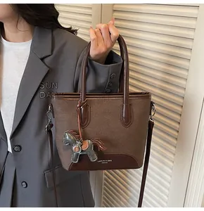 Detalle de un bolso tipo cubo marrón con colgante de caballo y costuras de tela texturizada
