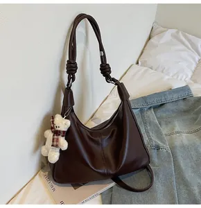 Deep brown matte leather tote bag with thick rope knot detail and plush bear charm