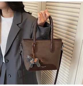 Detalle de bolso cubo en lona marrón y cuero con colgante de caballo y logotipo grabado