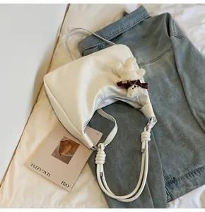 Detail of white PU leather hobo bag with woven strap and plush bear charm on soft fabric