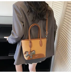 Detalle del bolso tipo cubo en marrón con un colgante decorativo de caballo de cuero al lado