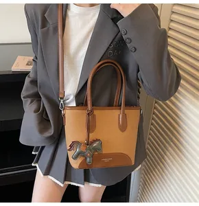 Detalle de bolso tipo cubo marrón con colgante de caballo y correa desmontable