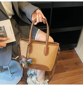 Detalle de un bolso cubo de tela caqui con asas de cuero marrón y colgante de caballo