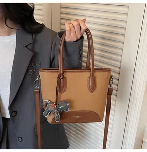 Detalle del bolso de lona tipo cubo con logo inferior y accesorio de poni gris