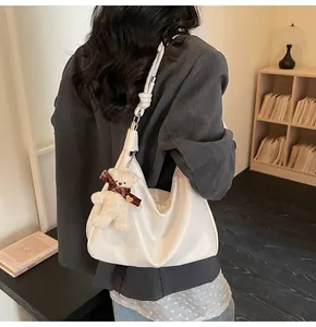 Detail of white half-moon hobo bag with shoulder strap knot and plush bear charm decoration