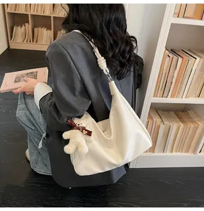 Detail of cream white leather hobo bag featuring woven knot strap and plush bear charm