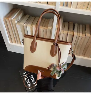 Detalle de bolso tipo cubo de lona con ribete de cuero y colgante de caballo