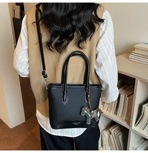 Detalle de bolso tipo cubo negro con colgante de caballo y correa de hombro de cuero