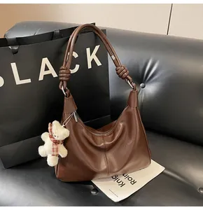 Detail of dark brown hobo bag with knotted shoulder strap and cute bear pendant