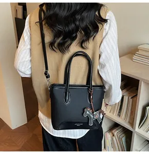 Detalle de un bolso tote negro minimalista con un colgante de caballo y logo de marca
