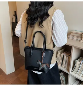 Detalle de bolso cubo de piel negra con colgante de caballo y logo de la marca
