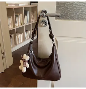 Deep brown leather hobo bag on a door handle featuring a cute plush bear charm accessory