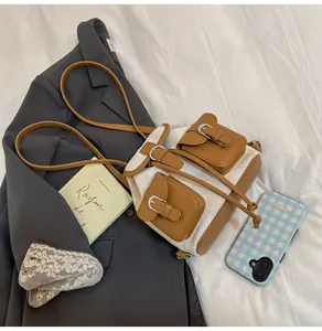 Detalle de mini mochila de lona con bolsillos de cuero marrón y hebillas metálicas