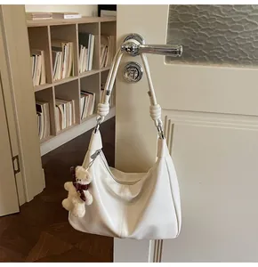 Off-white tote bag with bear charm hanging on door handle in a cozy home setting