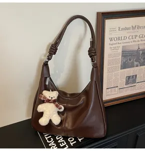 Detail of dark brown leather shoulder bag with knotted strap and cute bear charm