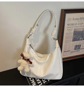 Detail of white matte hobo bag with knotted shoulder strap and plush bear pendant