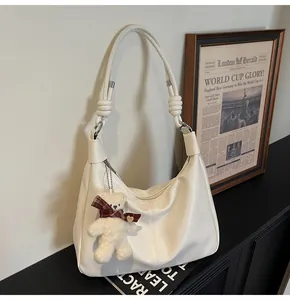 Close-up of a white leather hobo bag featuring a cute teddy bear charm and silver metal zipper