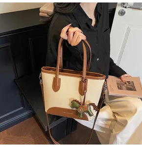 Detalle del bolso tipo cubo de lona con colgante de caballo verde y texto de moda
