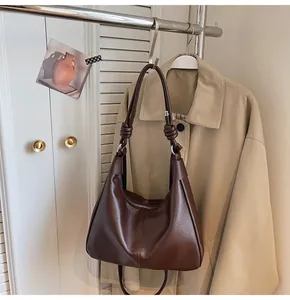 Detail view of the knotted shoulder strap on a brown leather tote bag in a home setting