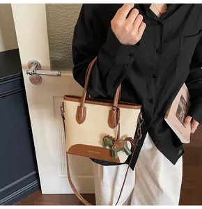 Bolso tipo cubo de lona y cuero marrón con colgante de caballo usado por una modelo