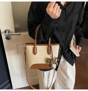 Detalle de bolso cubo de lona con ribete de cuero marrón, correa larga y colgante caballo
