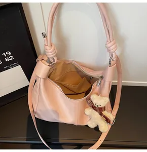 Detailed view of pink leather tote bag with knotted handles and a plush bear charm
