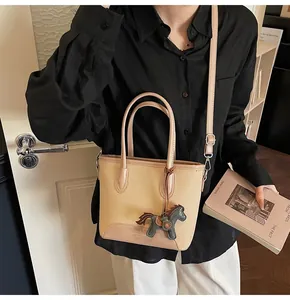 Detalle del bolso tipo cubo de lona beige con ribete de cuero rosa y colgante de caballo