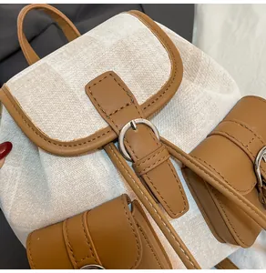 Detalle de mochila de lona beige con ribete de cuero marrón y hebilla de plata