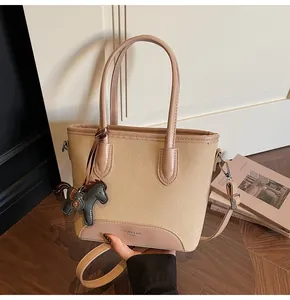 Detalle del bolso tipo cubo en lona caqui y cuero rosa con un colgante de caballo gris
