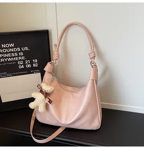 Detail of pink matte leather hobo bag with knotted handle and white teddy bear charm