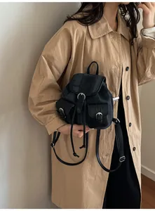 Detalle de una mini mochila de mezclilla negra con bolsillos sobre un abrigo beige