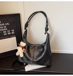 Detail of black faux leather shoulder bag with plush bear charm and stitch accents