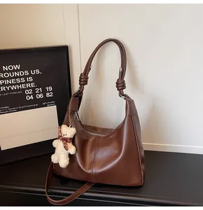 Close-up of brown hobo bag featuring knotted handle detail and a cute plush bear charm